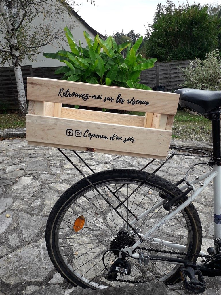 Porte bagage de vélo réalisé avec des fers à béton soudés et une caisse en bois avec le logo Copeaux d'un soir peint en noir